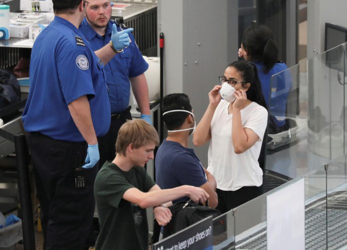 FILE PHOTO: Travelers wear mask as they go through security screening hours before travel restrictions are enacted on flights from Europe entering the U.S. because of concerns of the novel coronavirus at the Denver International Airport